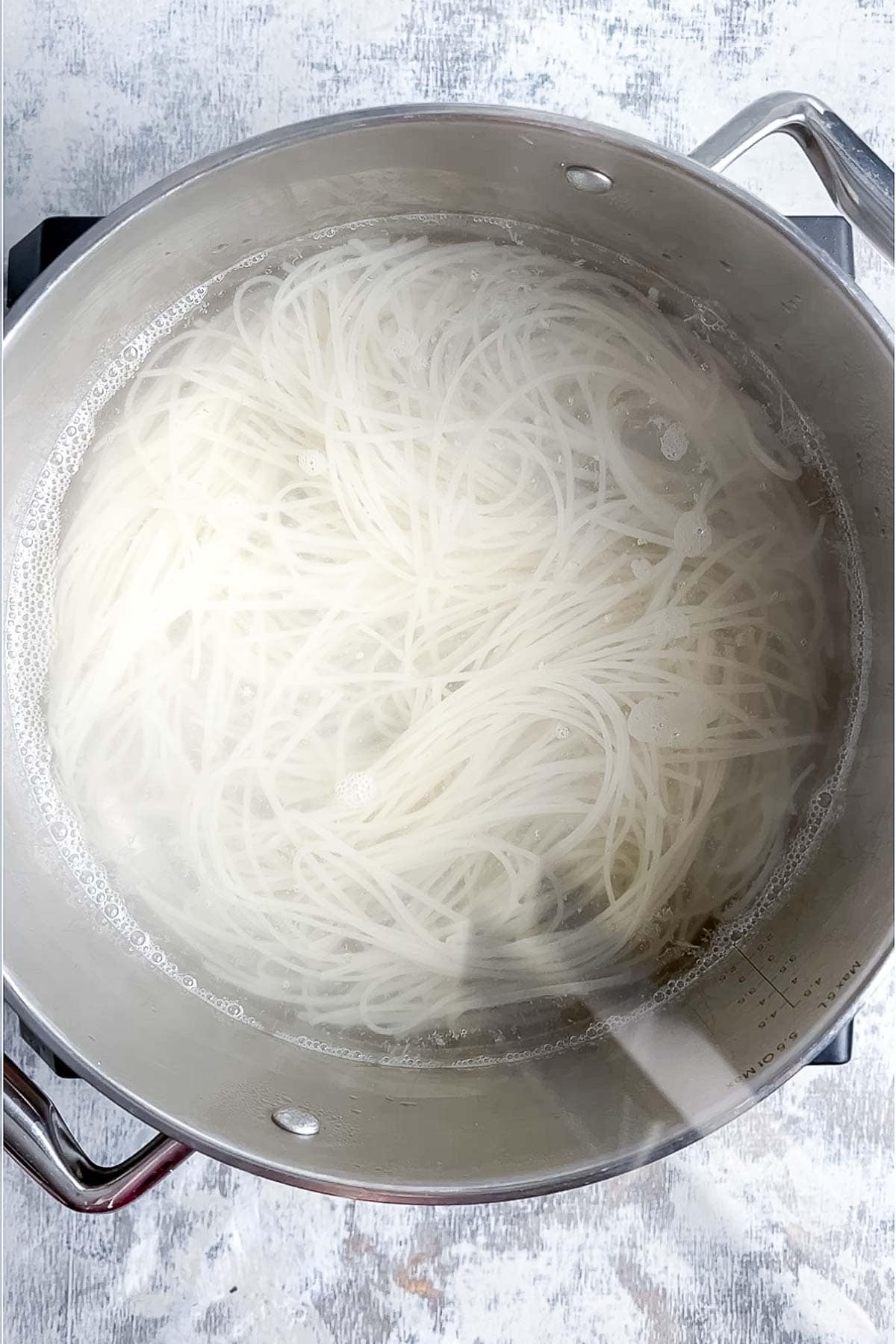 A pot of thin rice noodles boiling in water on a stovetop.