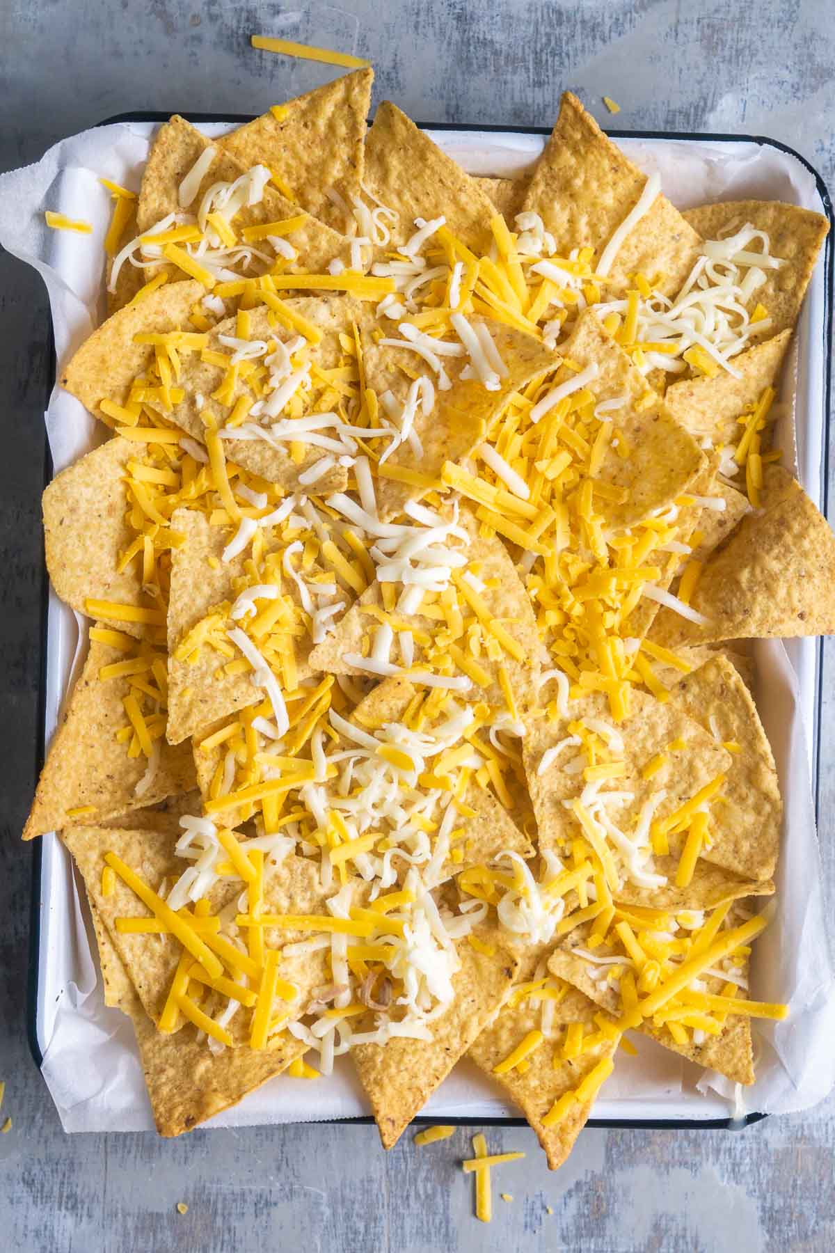 golden brown tortilla chips topped with shredded cheese on parchment-lined white baking sheet