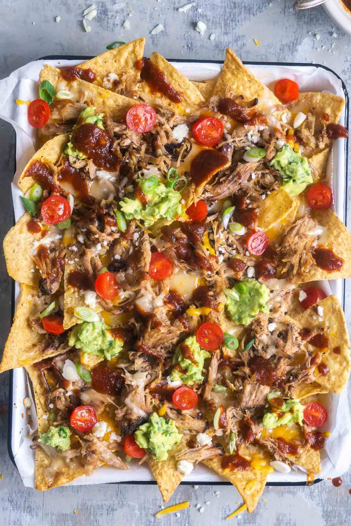 pulled pork nachos on parchment-lined white baking sheet