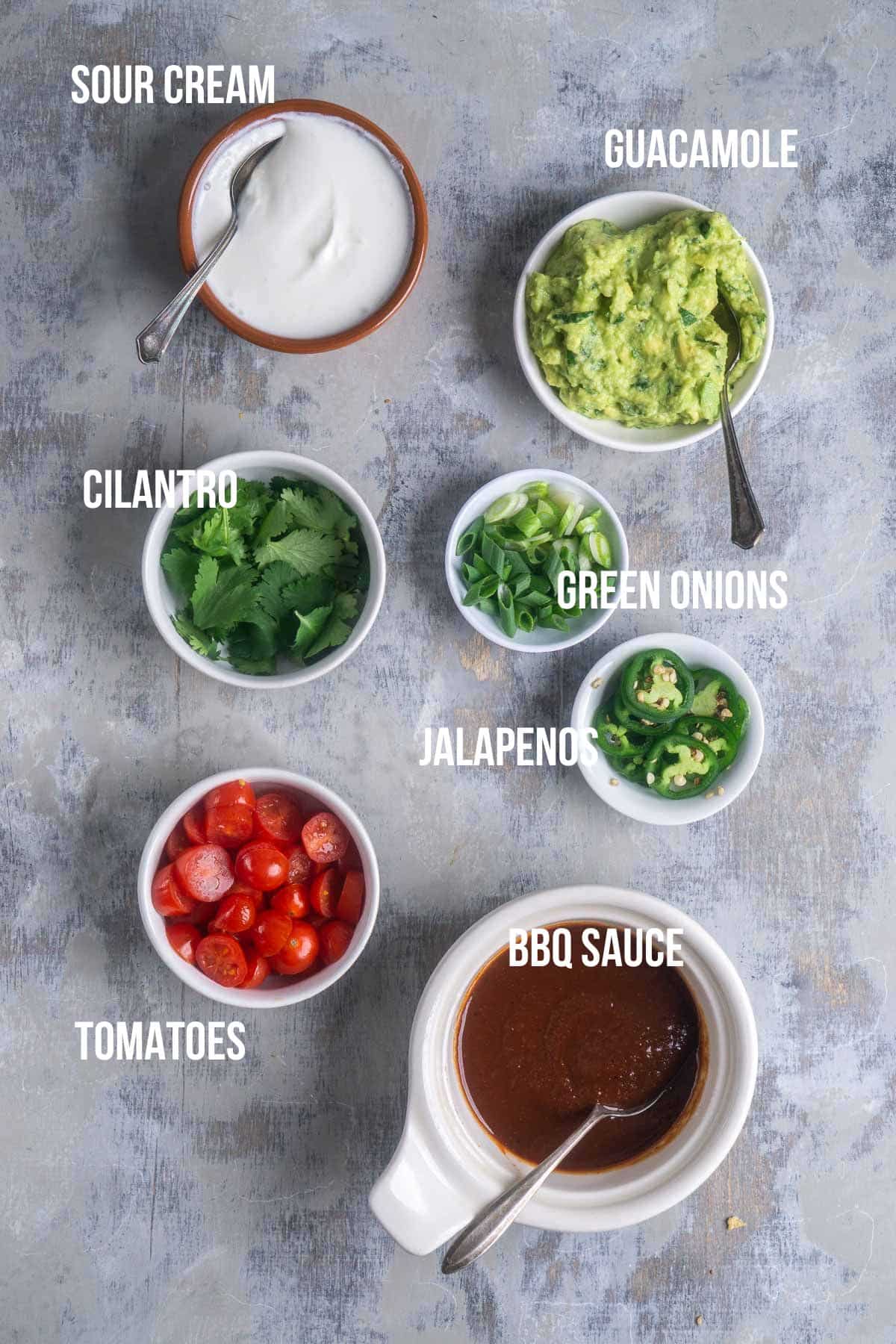 toppings for pulled pork nachos in small bowls with text overlay identifying each ingredient
