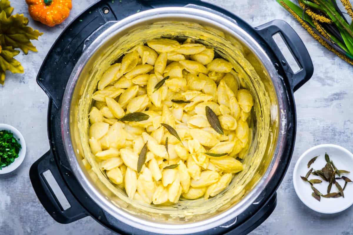 Pumpkin pasta in the Instant Pot next to garnish and autumn decorations