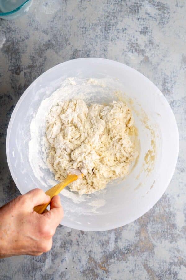 person's hand stirs dough ingredients in white bowl