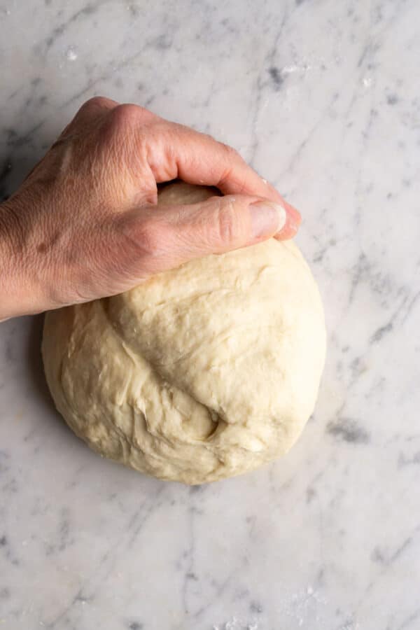 Persons hand kneads dough on white surface