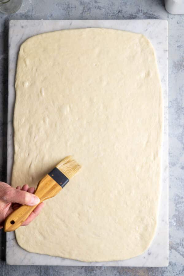 Persons hand brushing rolled out dough with pastry brush