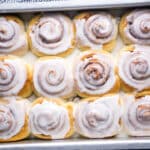 fluffy glazed cinnamon rolls in baking pan with striped linen