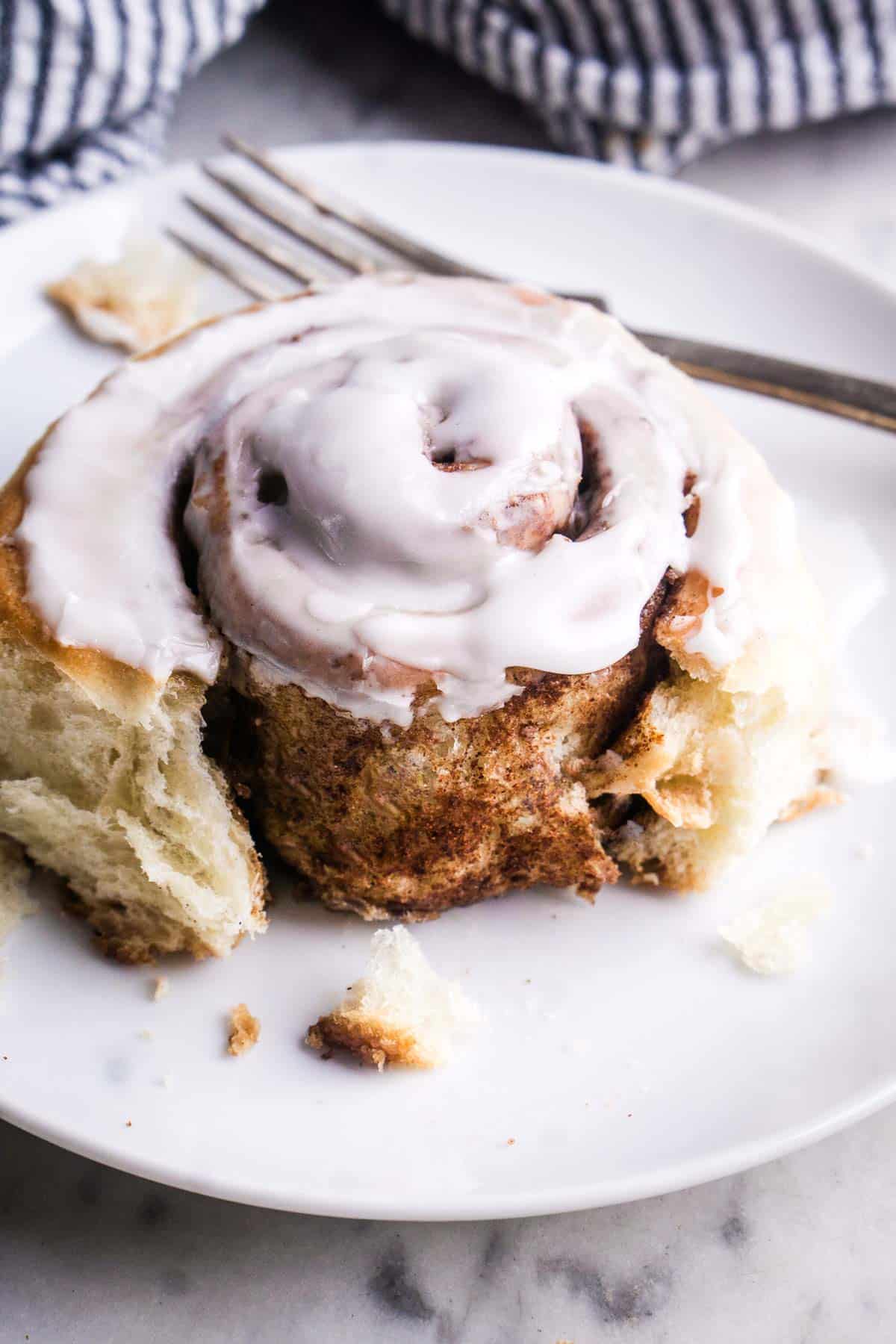 fluffy glazed cinnamon roll on white plate with fork