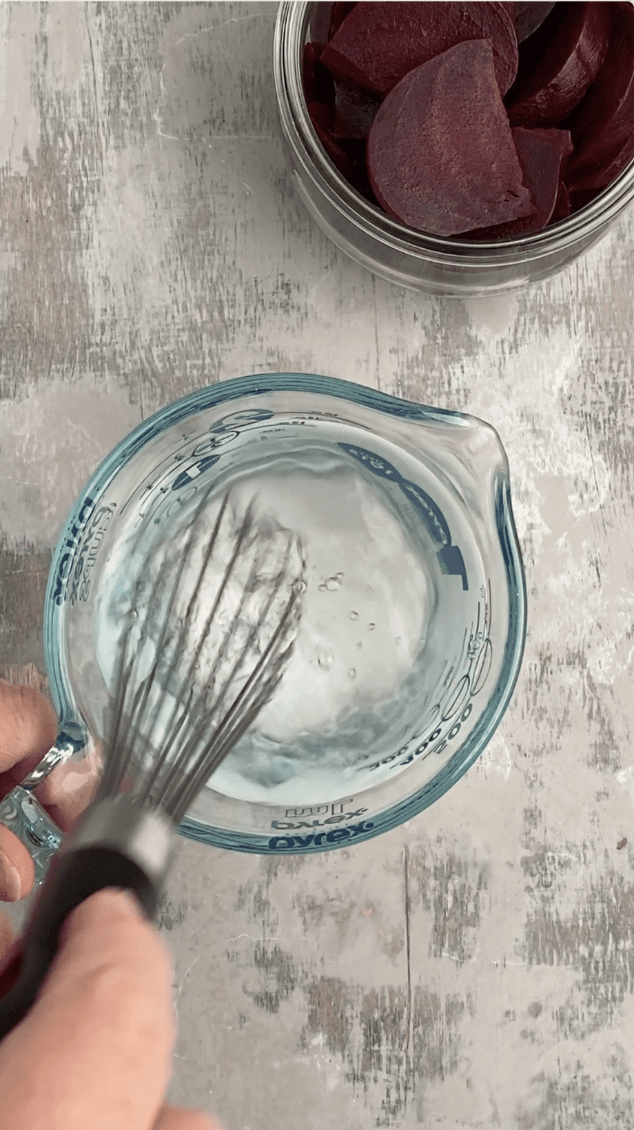 hand whisking pickling brine in glass measuring cup