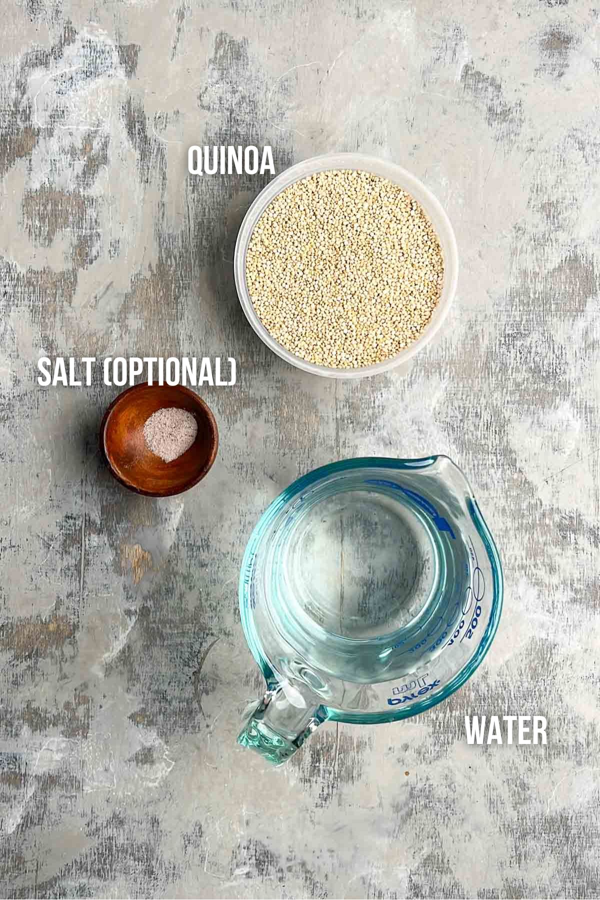 A bowl of uncooked quinoa, a small bowl of salt, and a measuring cup of water are arranged on a textured surface. Labels indicate each item.