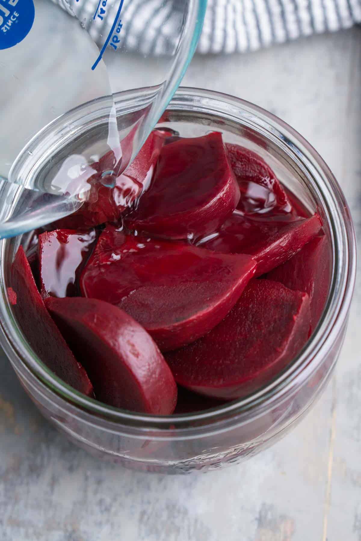 pickling brine is added to cooked sliced red beets in glass jar