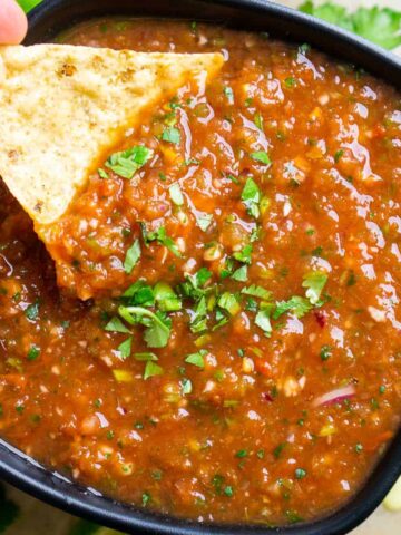 tortilla chip is dunked into blender salsa in a black bowl
