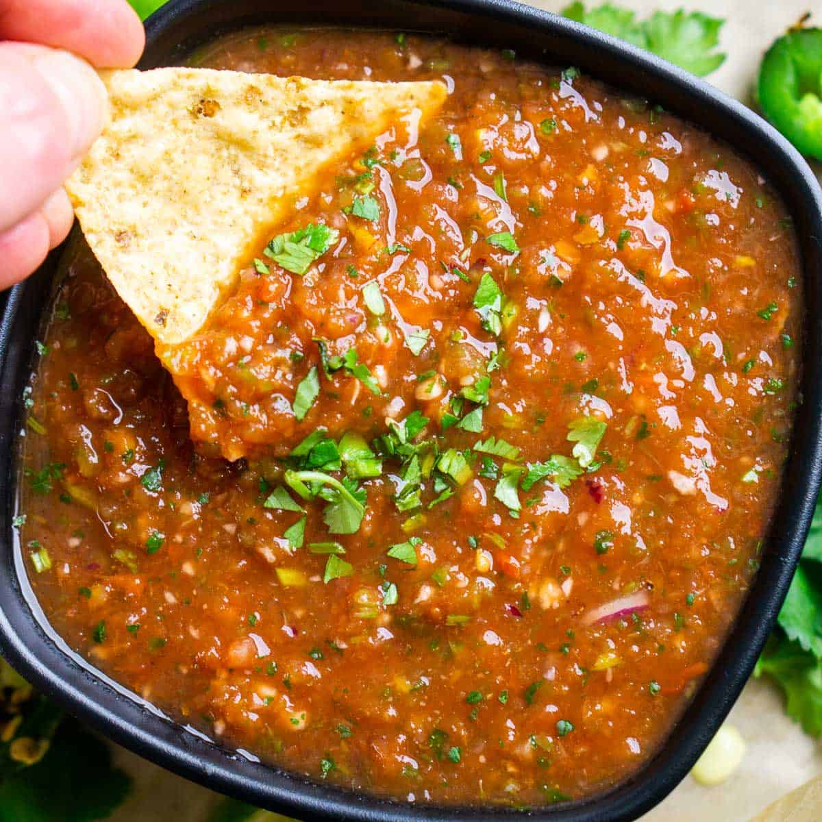 tortilla chip is dunked into blender salsa in a black bowl