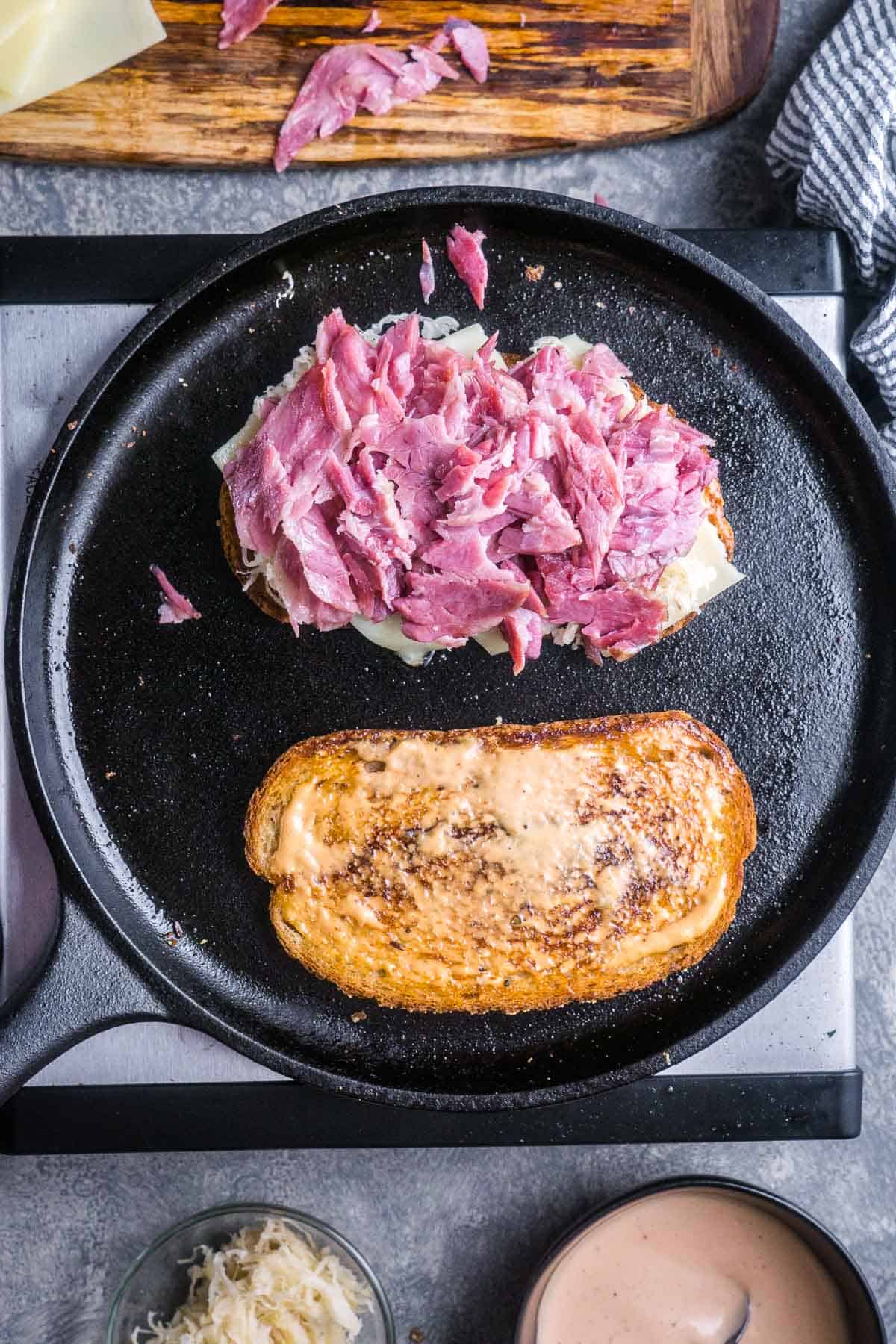 Two Reubens in a cast iron skillet, one opened to show sliced corned beef