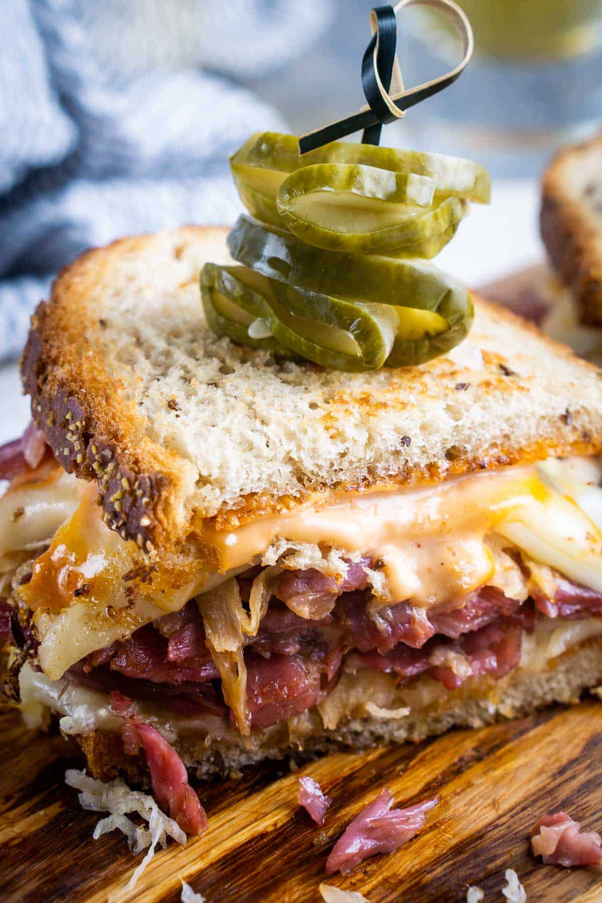 Half of a grilled Reuben sandwich on a cutting board, topped with sliced pickles