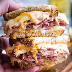 Closeup of hand holding two halves of a Reuben sandwich stacked on top of each other