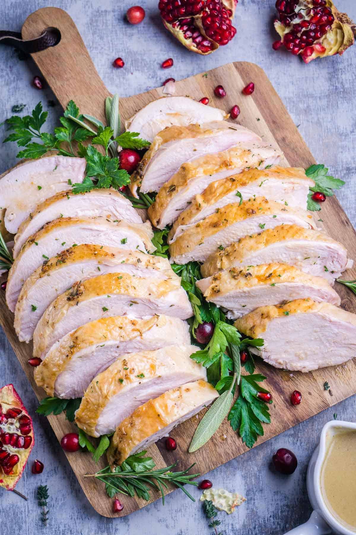 roast turkey breast slices on serving board garnished with fresh herbs, pomegranate, and cranberries