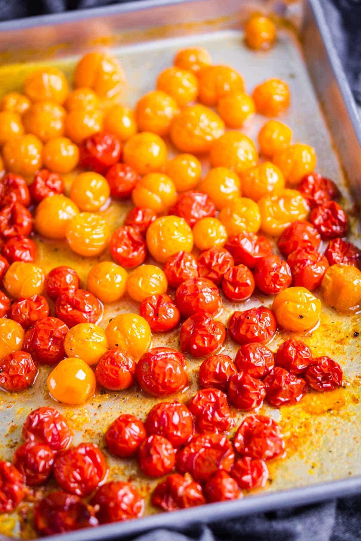 Red and yellow roasted cherry tomatoes on a baking sheet.
