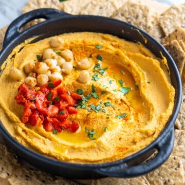 roasted red pepper hummus in black bowl on a platter of crackers