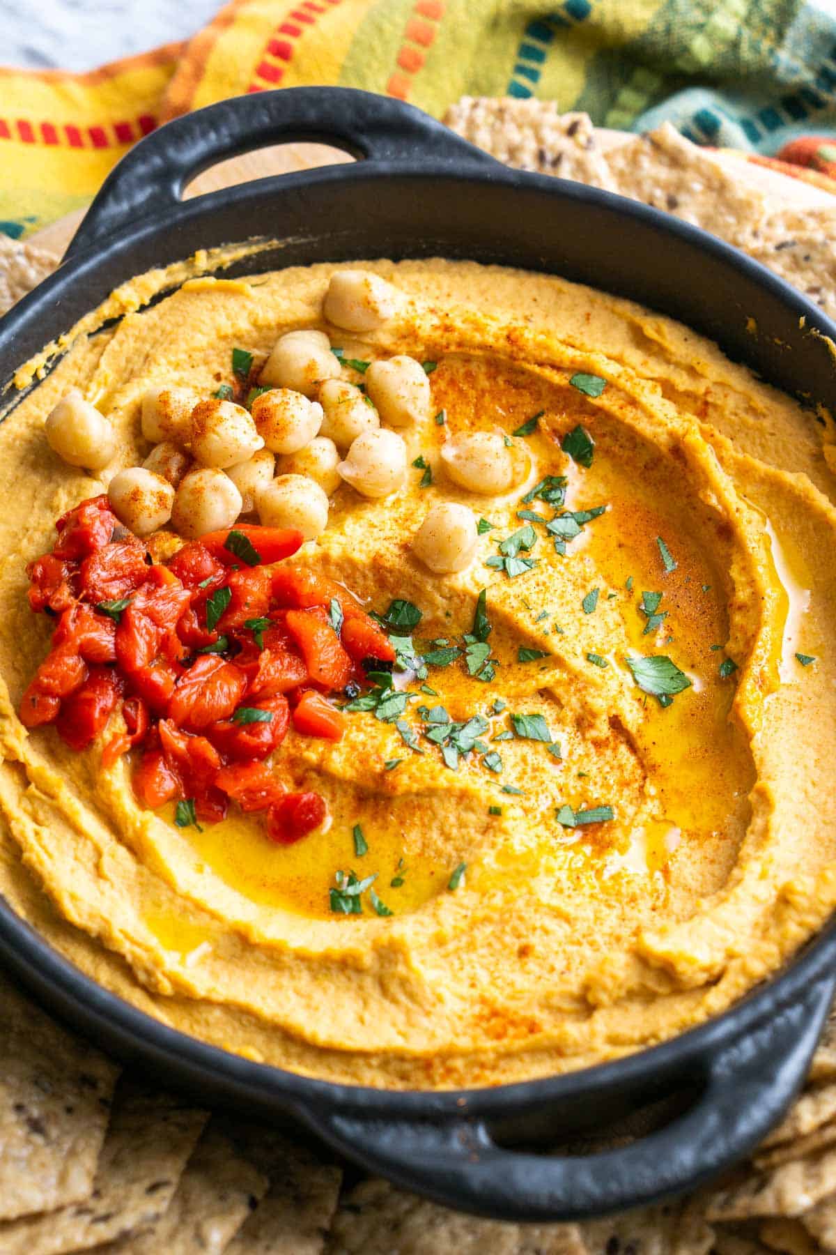 roasted red pepper hummus in black bowl on a platter of crackers