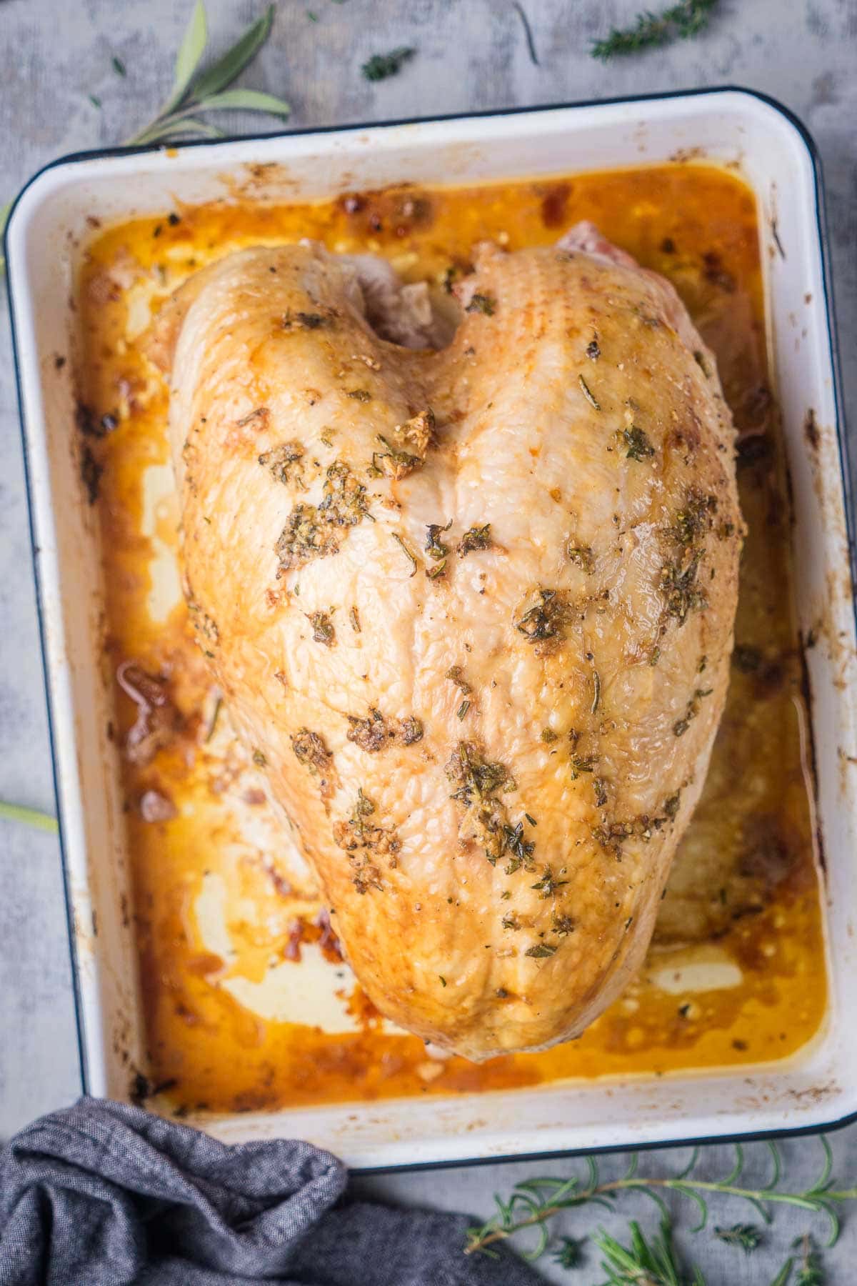 A golden brown, herb-seasoned roasted turkey breast in a baking dish.