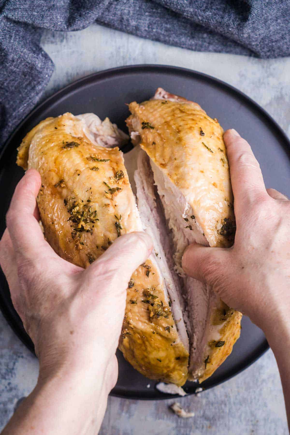 two hands separate baked turkey breast meat from cavity