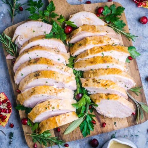 roasted turkey breast slices displayed on wood cutting board garnished with fresh parsley and fresh cranberries