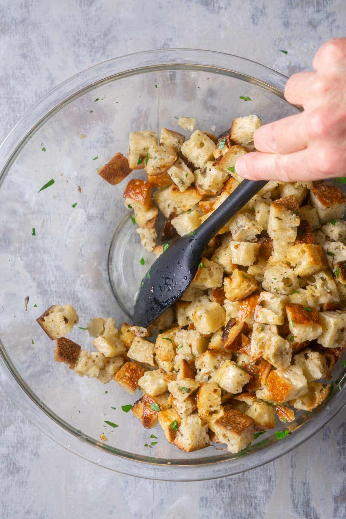 black spoon stirs bread stuffing cubes with broth mixture