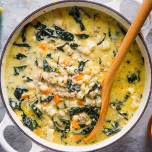 Sausage kale white bean soup in white soup pot with wooden soup ladle.