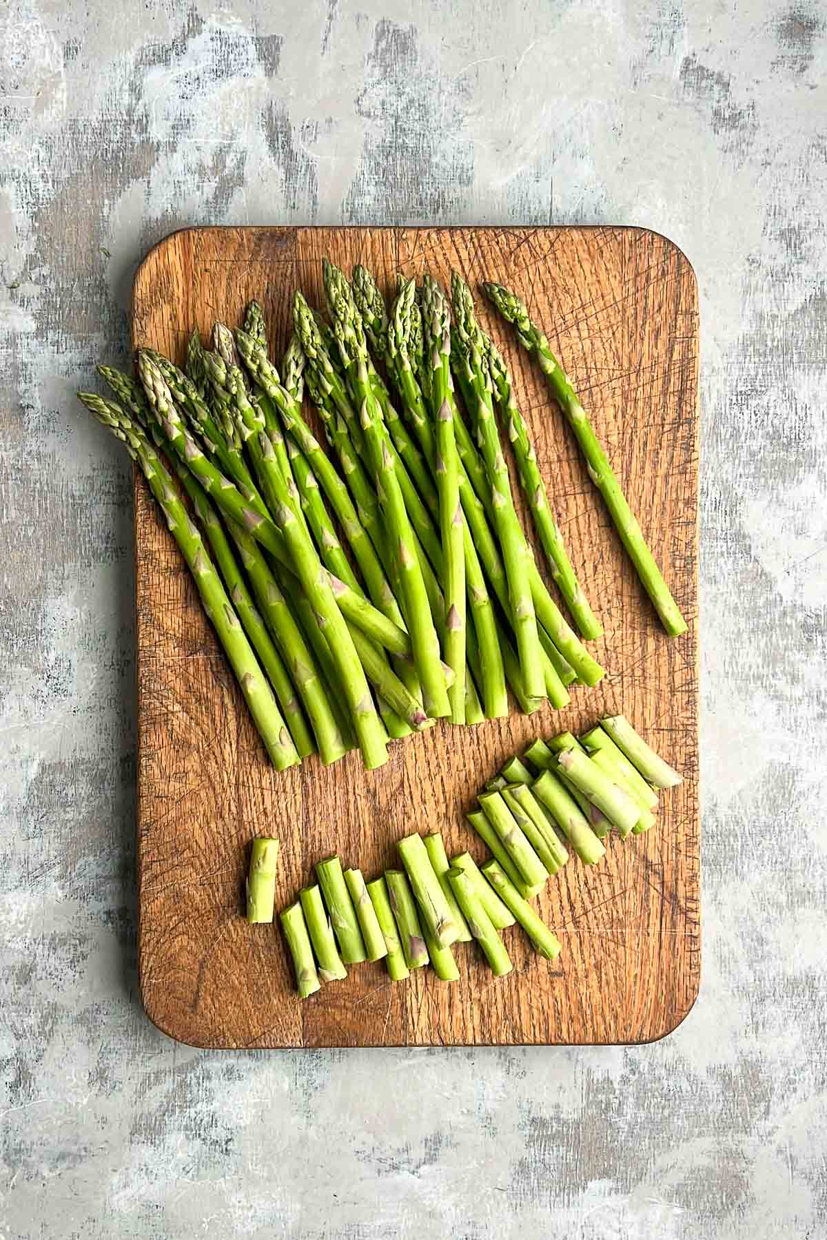 A bundle of asparagus spears, some whole and some chopped, arranged on a wooden cutting board.
