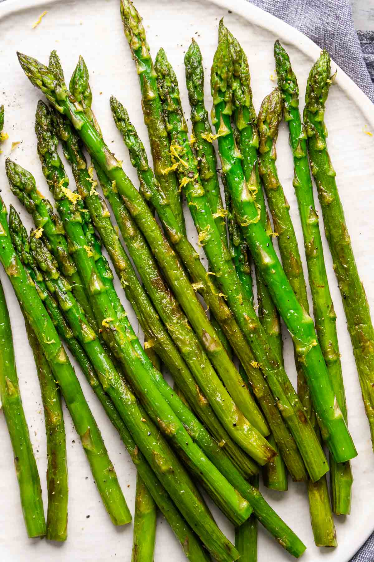 Sautéed asparagus is a simple vegetable side dish that's ready in minutes and uses minimal olive oil. It’s perfectly tender, flavorful, and completes almost any entree. Great for snacking too! Sauteed asparagus spears arranged on a white plate, garnished with lemon zest.
