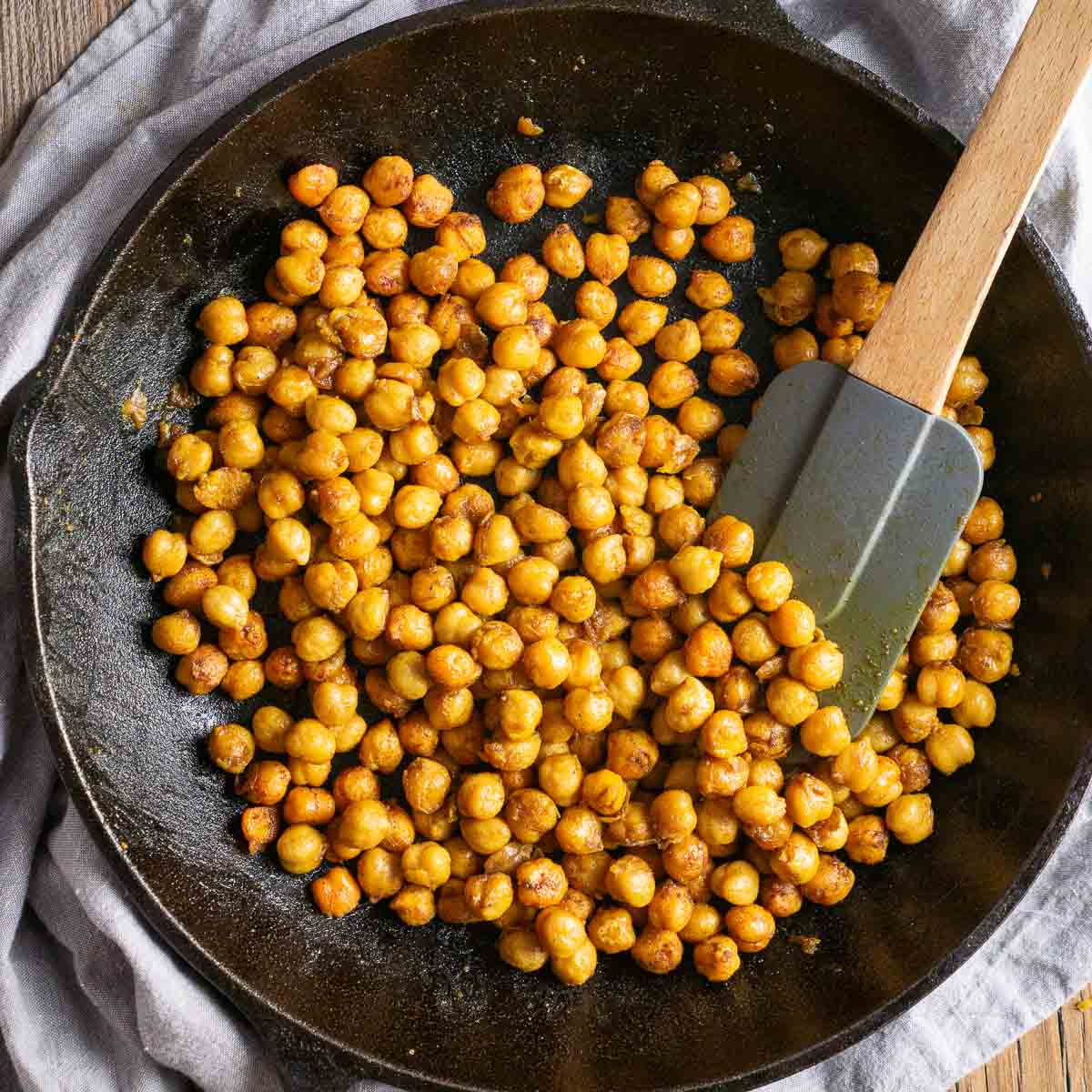 sauteed chickpeas in cast iron skillet with silicone spatula on gray linen