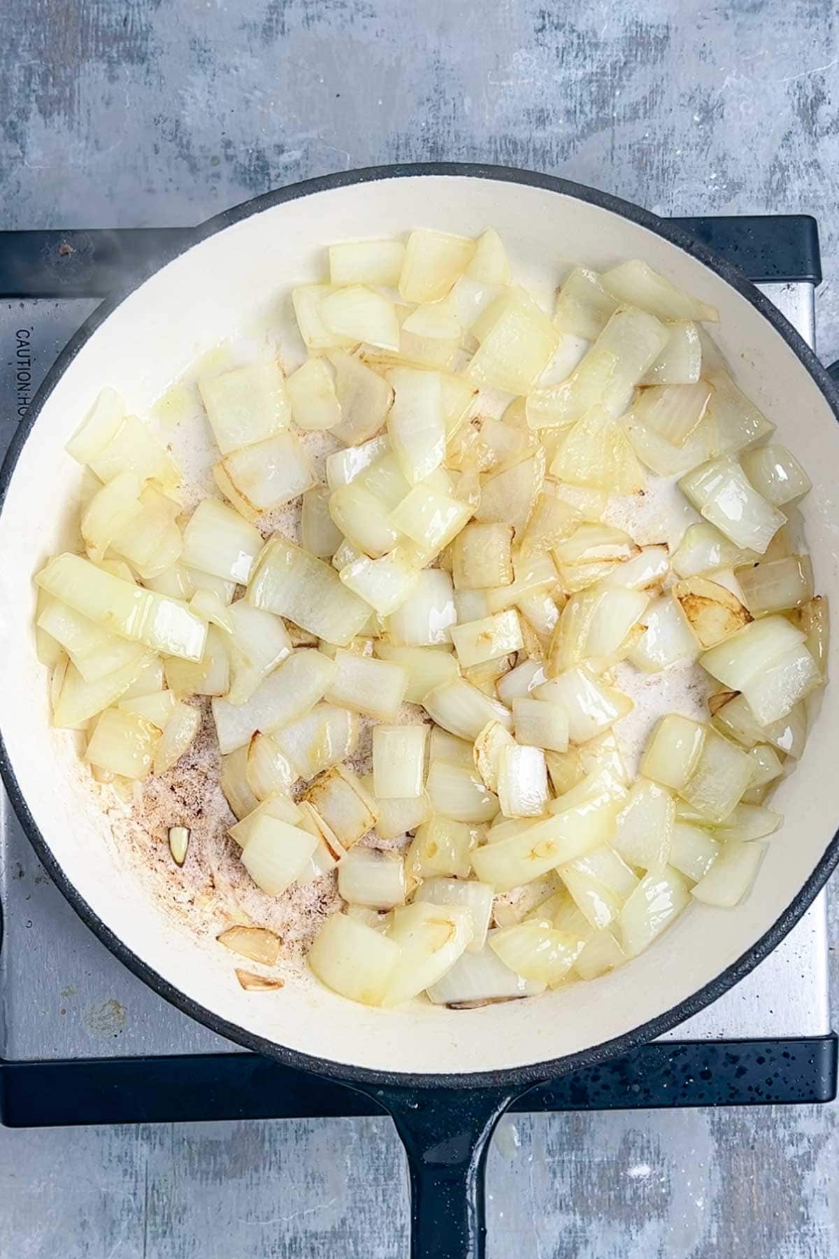 Diced onions being sautéed in a white frying pan on a stove.