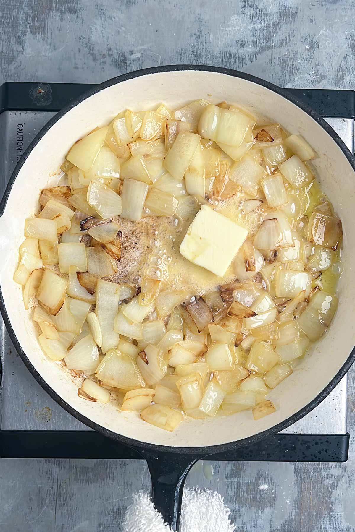 Chopped onions being sautéed in butter in a white pan on a stovetop.