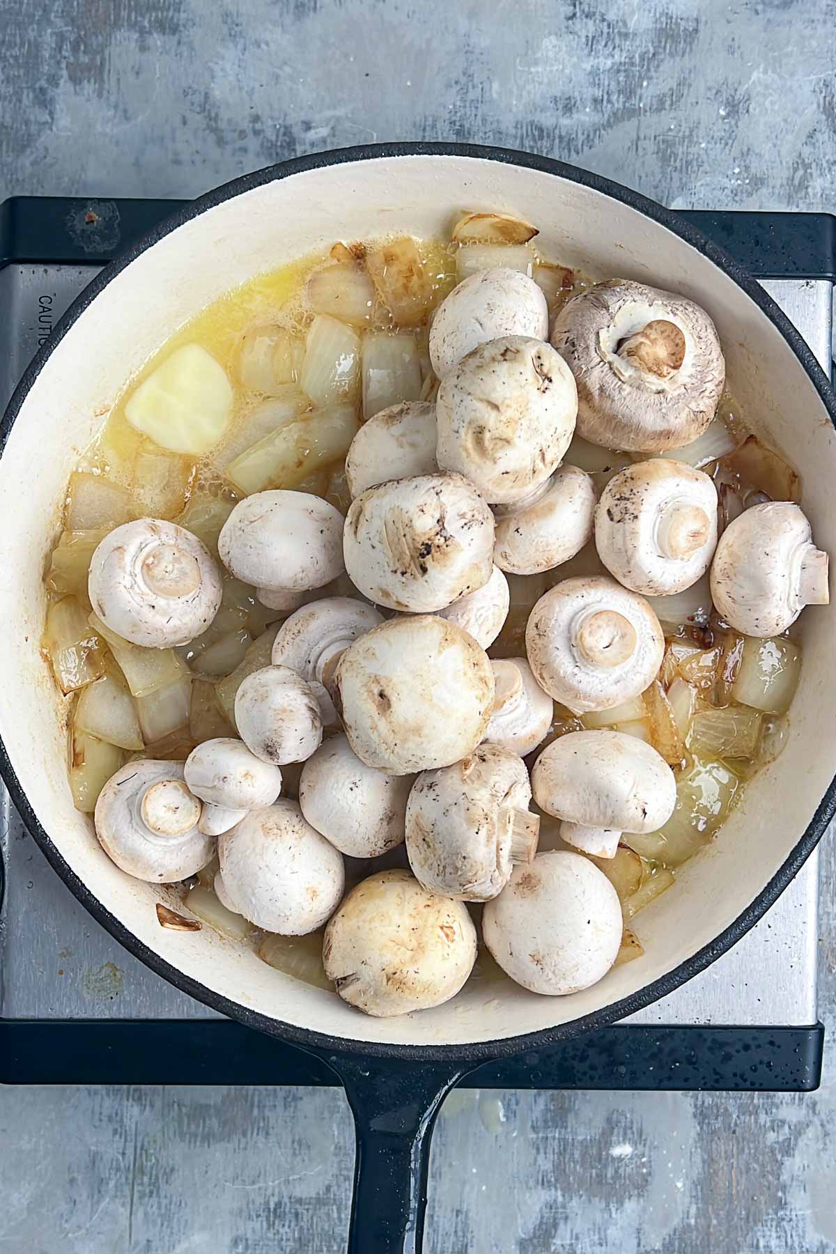 White mushrooms and diced onions cooking in a pan on a stovetop.