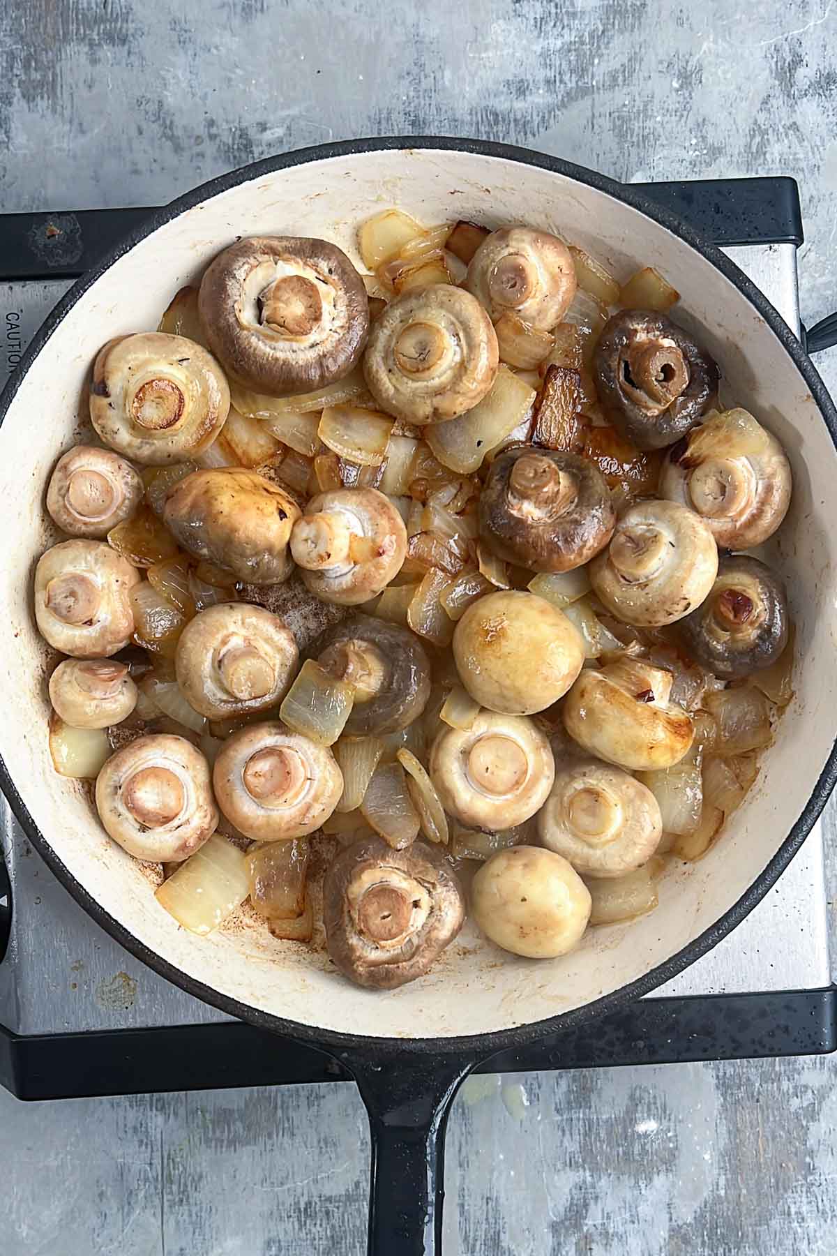 Sautéed mushrooms and onions in a pan on a stovetop.
