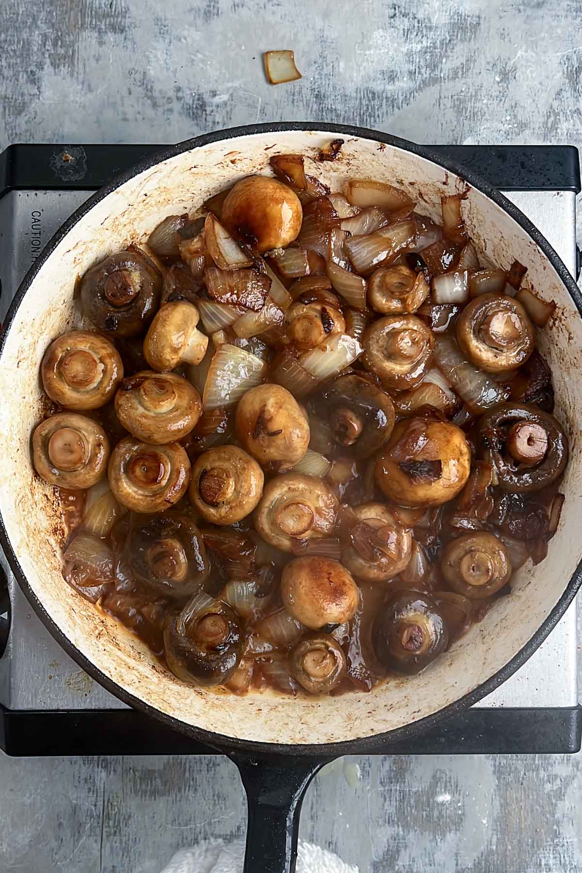 Mushrooms and onions are being sautéed in a pan, with a lightly browned surface and some steam visible.