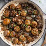 Cooked mushrooms and onions in a skillet, garnished with chopped herbs.