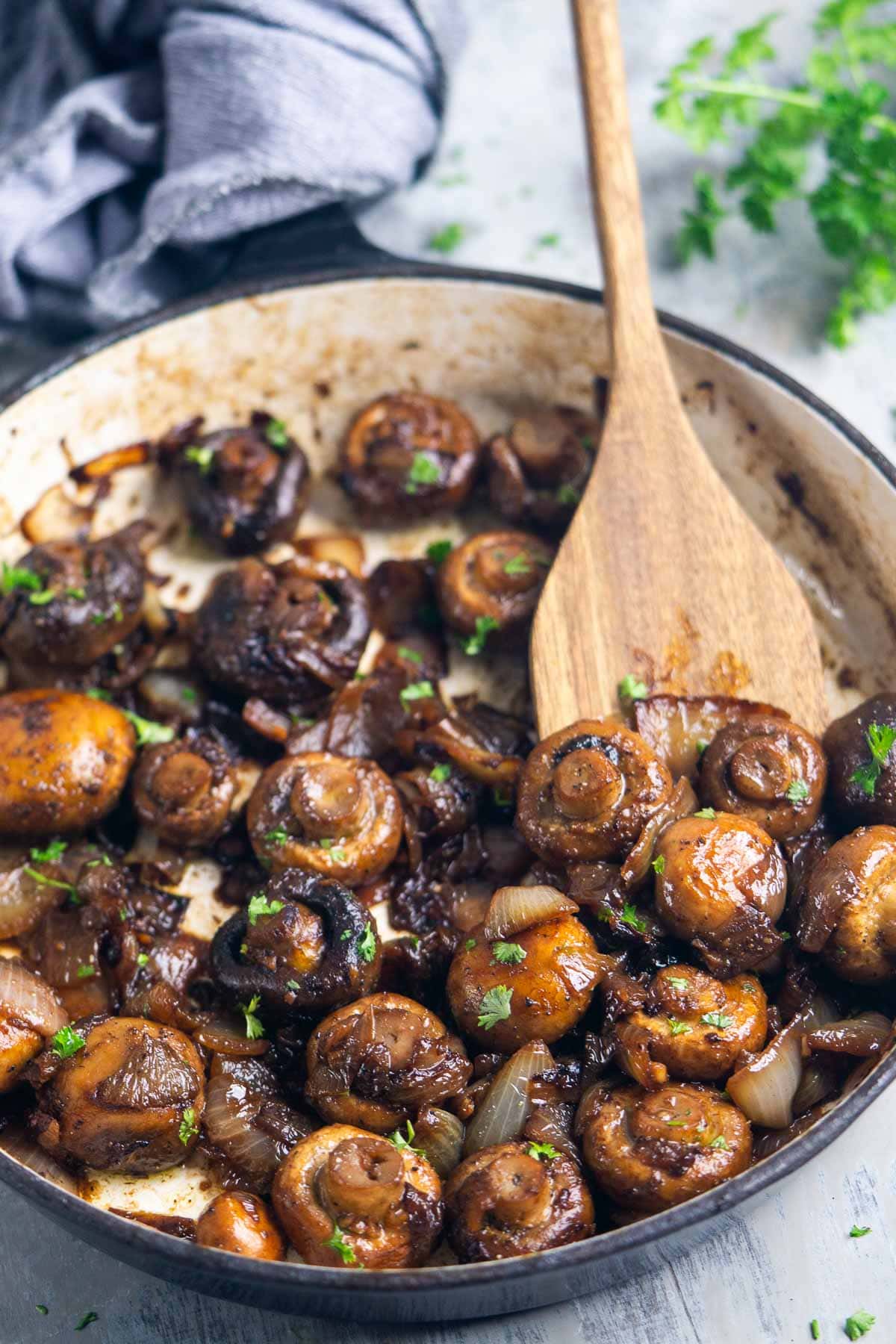 Sautéed mushrooms and onions in a pan, garnished with chopped parsley, with a wooden spatula scooping up mushrooms.