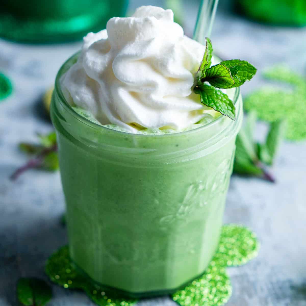 shamrock shake in glass parfait jar topped with whipped cream, mint garnish, and clear straw