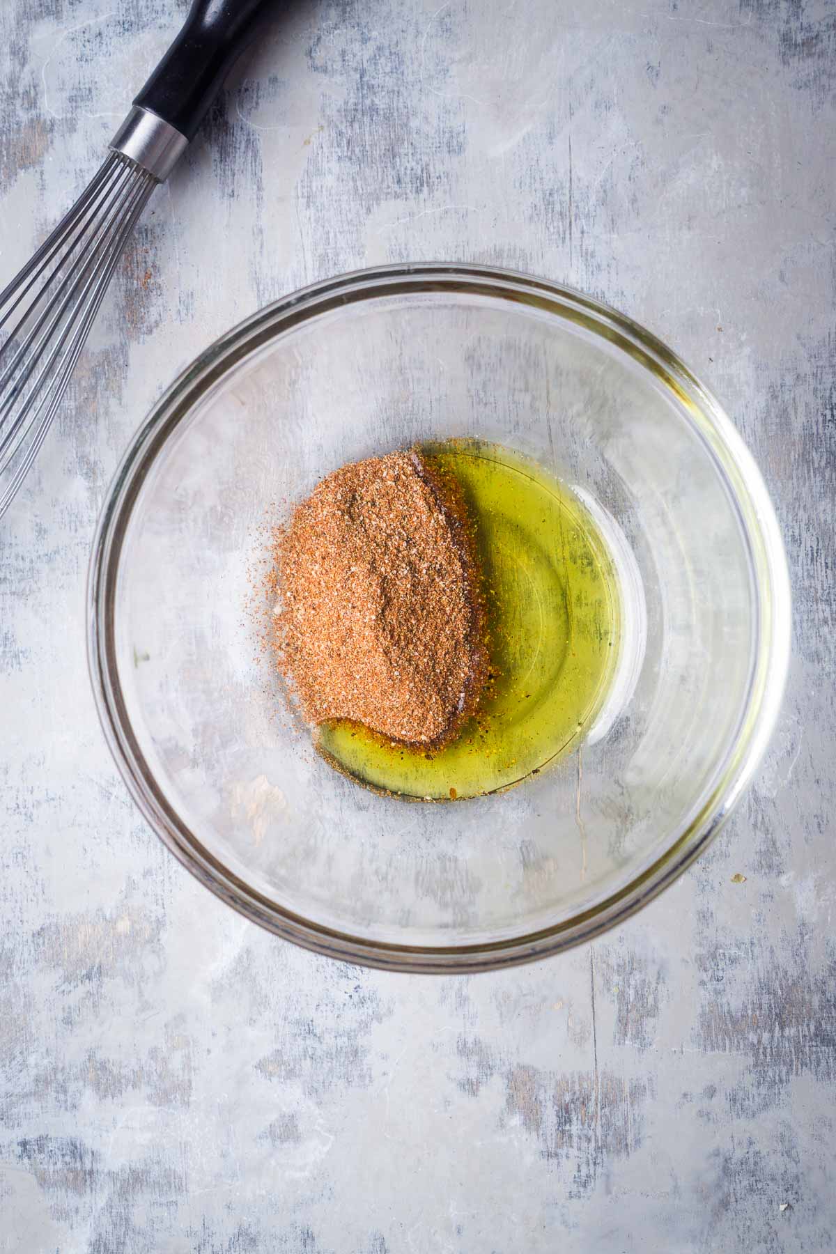 OIl and fajita seasoning in glass mixing bowl next to whisk.