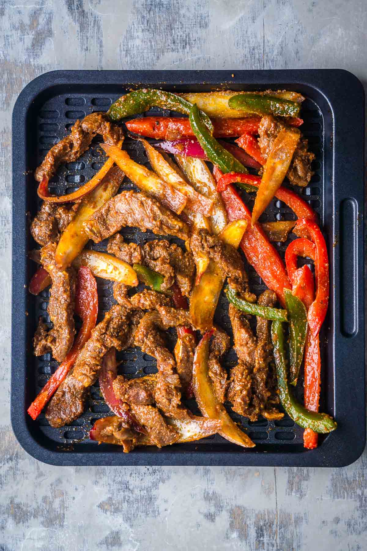 Seasoned steak, bell peppers, and onions on a baking sheet.