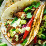 Steak fajitas in flour tortillas topped with guacamole, salsa, and cilantro.
