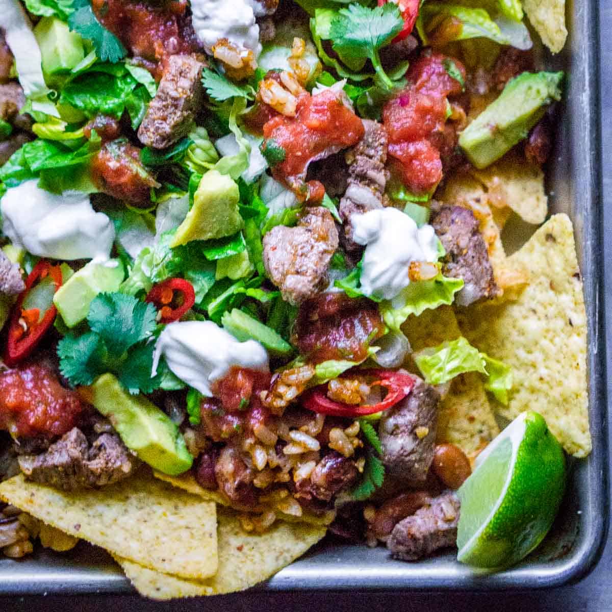 steak nachos on baking sheet with a lime wedge