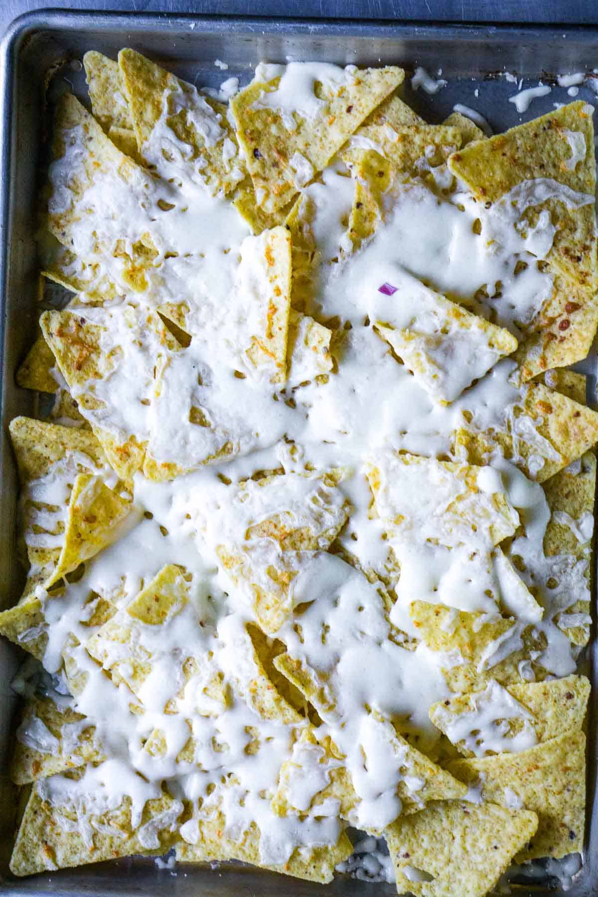 tortilla chips covered with melted cheese on baking sheet