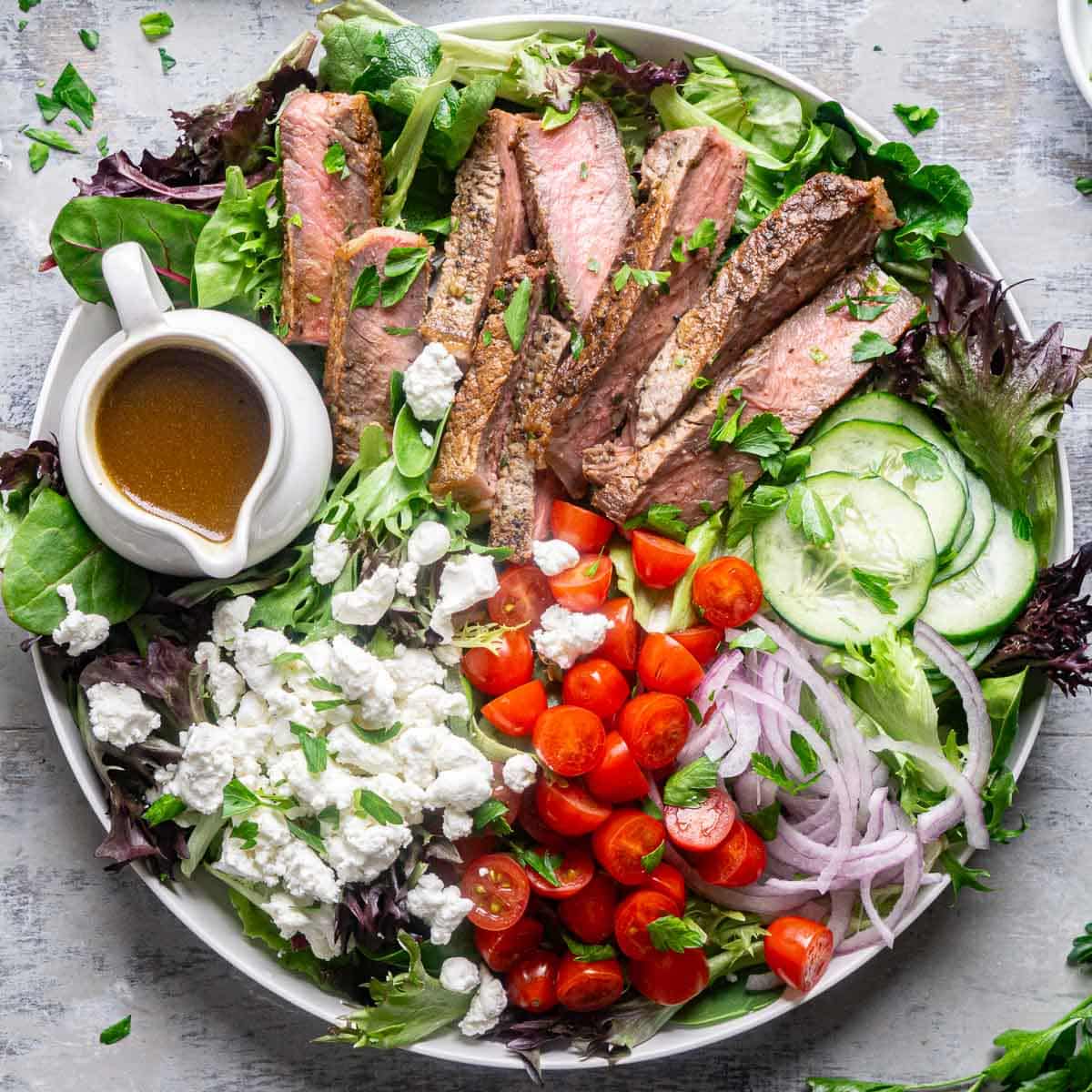 steak salad on white plate with white container of balsamic dressing