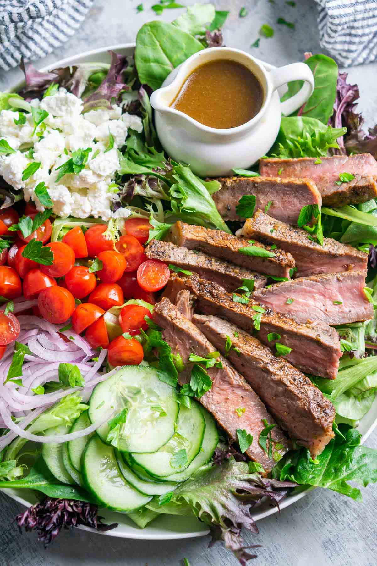 steak salad on white plate with white container of balsamic dressing