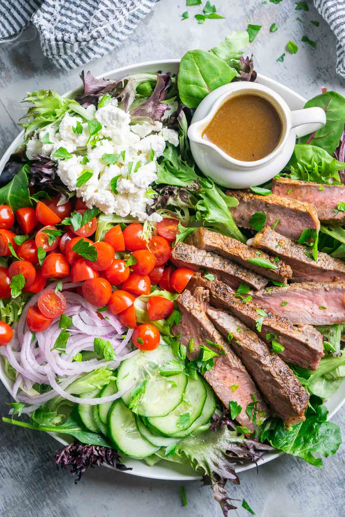 steak salad on white plate with white container of balsamic dressing