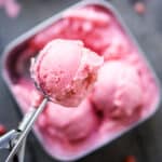 ice cream scoop picks up a scoop of strawberry frozen yogurt from stainless storage container