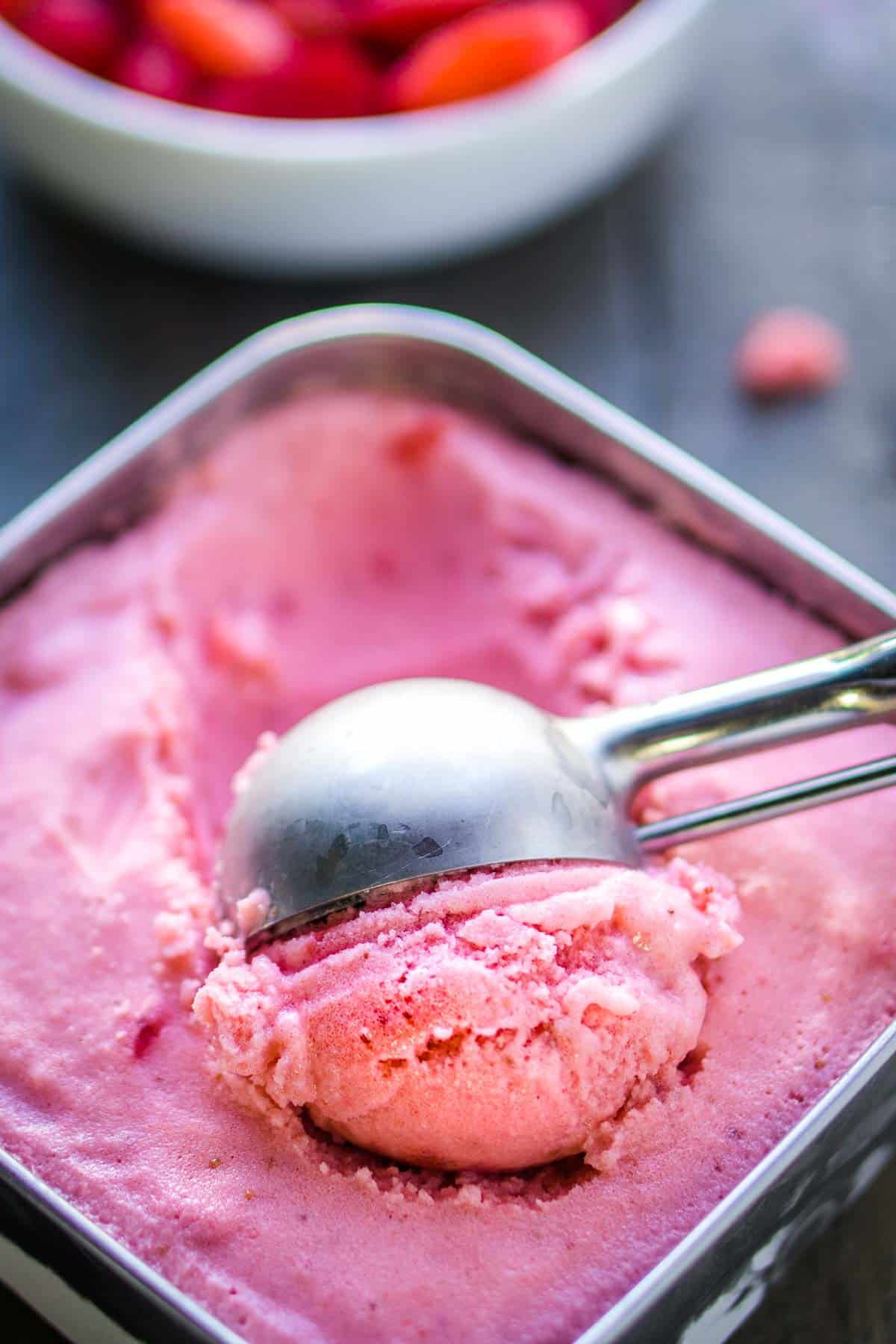 ice cream scoop is scooping strawberry frozen yogurt from stainless storage container
