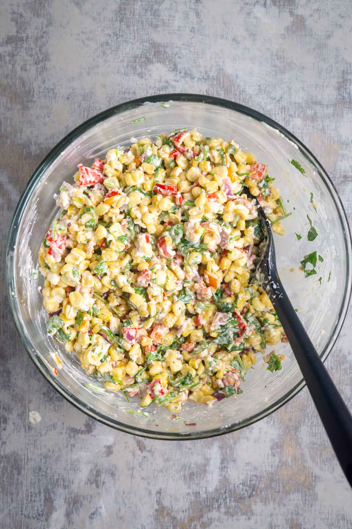 Street corn salad in glass mixing bowl with black spatula.
