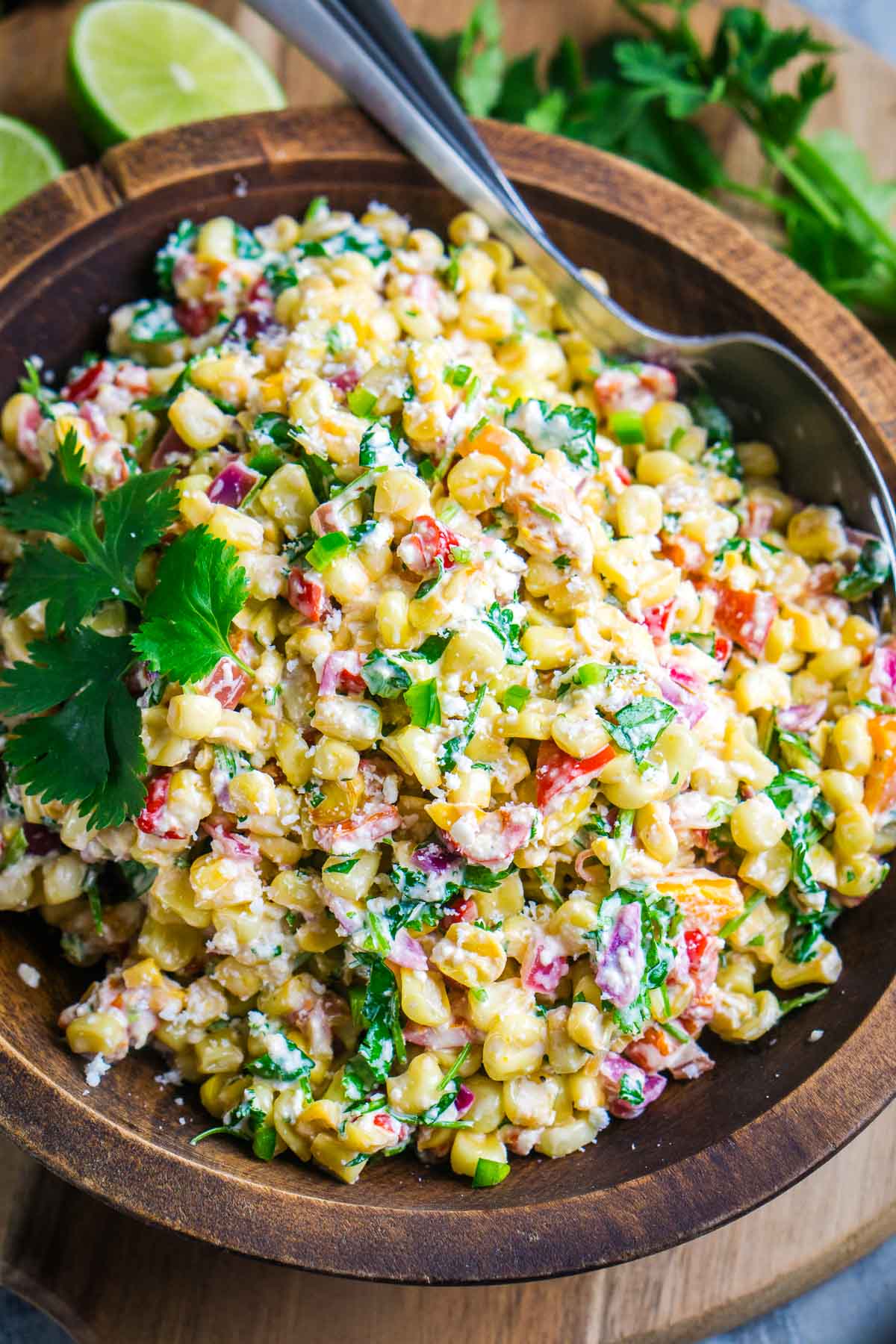 Street corn salad in brown serving bowl with serving utensils.